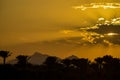 Golden tropical sunset over silhouette of palm trees and mountains. Sun`s rays break through clouds. Magnificent landscape Royalty Free Stock Photo