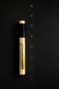 Golden tube for mascara, black paper background, glare of light on the background, closed tube of mascara
