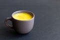 Golden turmeric milk in a gray cup on the dark background.