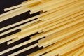 Golden uncooked spaghetti lie on a black wooden background. Minimalism