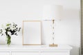 Golden vertical frame and bouquet of fresh flowers on white furniture, luxury home decor and design for mockup creation