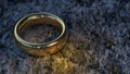 A golden wedding ring lies on the gray, dirty ground under the yellow glow.