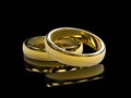 Golden wedding rings on black background and reflective table Royalty Free Stock Photo