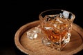 Golden whiskey in glass with ice cubes on wooden barrel