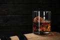 Golden whiskey in glass with ice cubes on wooden barrel.