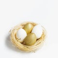 Golden and white colors eggs in straw nest on white background. Stylish bright egg for easter spring holiday. Decorative Royalty Free Stock Photo