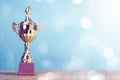 Golden winner`s trophy on sky background standing on wooden desk festive bokeh blur background