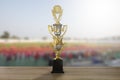 Golden winner trophy cup on wooden table on blurred sport stadium background with crowd