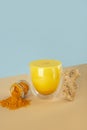Golden yellow milk with turmeric powder in a glass on with ginger on a isometric diagonal projection blue and beige background.