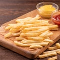 Golden yummy deep French fries on kraft baking sheet paper and serving tray to eat with ketchup and yellow mustard, top view,