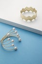 Golden zigzag shape bracelet on white surface and golden bracelet with pearls on blue Royalty Free Stock Photo