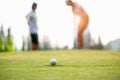 Golf ball approach to the hold on the green. Couple golf player putting golf ball in the background. Royalty Free Stock Photo
