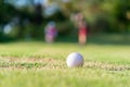 Golf ball approach to the hold on the green. Couple golf player ptiching golf ball in the background. Royalty Free Stock Photo