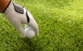 Golf ball in gloved hand, green course lawn background, close up view