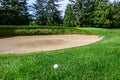 Golf ball in the grass rough in front of a sand trap, green and flag behind hazard Royalty Free Stock Photo