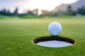 Golf ball lies near hole edge waiting for successful putt at sunset closeup. Exciting moment for golf players looking Royalty Free Stock Photo