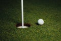 Golf ball nearby hole with pin flag, green grass background Royalty Free Stock Photo