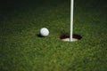 Golf ball nearby hole with pin flag, green grass background Royalty Free Stock Photo