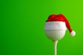 Golf ball in a red Santa Claus hat mounted on a tee. Sports concept on the theme of Christmas and New Year. Green background. Copy Royalty Free Stock Photo