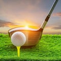 a golf ball sitting on top of a tee next to a wooden golf club. The scene is set on a golf course at sunset.close-up view Royalty Free Stock Photo