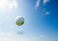 A golf ball is suspended mid-air against a clear blue sky, suggesting motion. The ball\'s surface Royalty Free Stock Photo