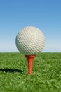 A golf ball on a tee against a clear blue sky, set in a lush green field Royalty Free Stock Photo