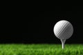 Golf ball with tee on artificial grass against black background Royalty Free Stock Photo