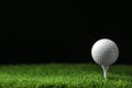 Golf ball with tee on artificial grass  black background, space for text Royalty Free Stock Photo