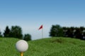 A golf ball on a tee with a flag in the background, set against a clear blue sky. Royalty Free Stock Photo