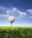 Golf ball on tee with grass, blue sky and clouds Royalty Free Stock Photo