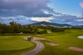 Golf cart on a golf course. Green field and cloudy blue sky. Spring landscape with grass and trees. Royalty Free Stock Photo