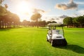 Golf cart in fairway of golf course with green grass field with cloudy sky and trees at sunset Royalty Free Stock Photo