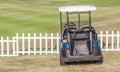 Golf cart parks near the white wooden fence around the golf course. Royalty Free Stock Photo