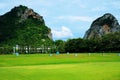 Golf driving range with green grass, trees, and mountain background under cloudy blue sky 2 Royalty Free Stock Photo