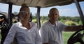 Golf players looking camera at cart. Couple sitting buggy on club course field. Royalty Free Stock Photo