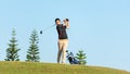 Golfer asia man approach on tee off for swing and hitting golf ball on slope green and looking fairway in course. Royalty Free Stock Photo