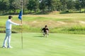 Golfer asian man with friend playing aiming shot for putting ball on the hole with club on green course. Royalty Free Stock Photo