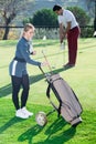 Golfer examining clubs while male hitting ball Royalty Free Stock Photo