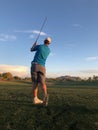 Golfer hitting a golf ball from a back view.