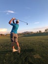 Golfer hitting a golf ball from a back view.