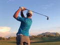 Golfer hitting a golf ball from a back view.