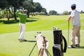 Golfer holding hole flag for friend putting ball Royalty Free Stock Photo