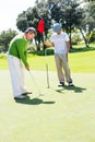 Golfer holding hole flag for friend putting ball Royalty Free Stock Photo