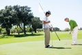 Golfer holding hole flag for friend putting ball Royalty Free Stock Photo