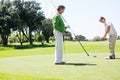 Golfer holding hole flag for friend putting ball Royalty Free Stock Photo