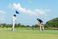 Golfer man and friend playing golf aiming shot for putting ball on the hole with club on green course. Royalty Free Stock Photo