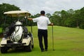 A golfer standing next to a golf cart looks at the golf course to plan the game Royalty Free Stock Photo