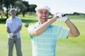 Golfer swinging his club with friend behind him Royalty Free Stock Photo