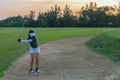 Golfer woman chip golf ball out of a sand trap. People swing and hitting golf course is on the fairway in sunset Royalty Free Stock Photo