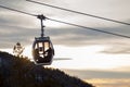 A gondola cableway with a booth suspended on a cable in which a couple in love sits on a background of mountains, trees and sunset